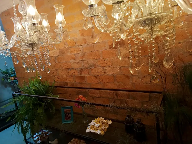 Lustres de cristal diante de uma parede de tijolos aparentes, com samambaias e uma mesa de doces